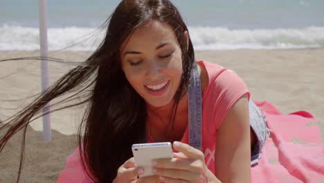 Woman-laying-on-beach-using-cell-phone