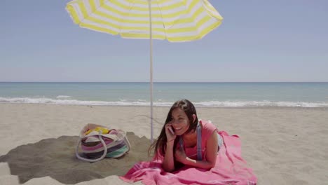 Woman-on-phone-call-at-beach-under-umbrella