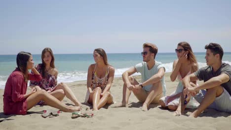 Gruppe-Von-Sechs-Freunden,-Die-Im-Sand-Am-Strand-Sitzen