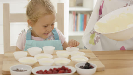 Lachendes-Mädchen-Mit-Muffinförmchen-und-Elternteil-In-Schürze