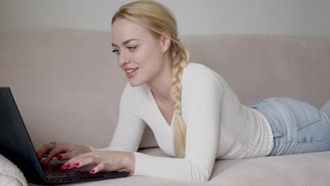 Blonde-Frau-Liegt-Auf-Dem-Sofa-Und-Surft-Am-Laptop