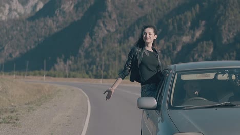 elated-lady-sits-on-blue-speeding-car-and-raises-hand-to-sky