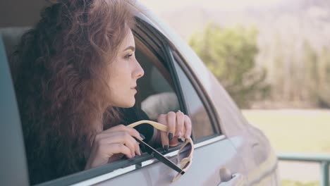 Die-Lockige-Frau-Hält-Eine-Sonnenbrille-In-Der-Hand-Und-Schaut-Aus-Dem-Autofenster