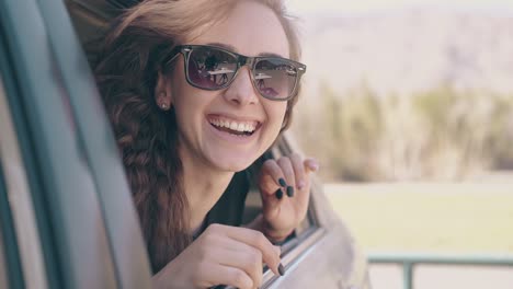 Positive-Frau-Setzt-Sonnenbrille-Auf-Und-Repariert-Haare-Im-Auto