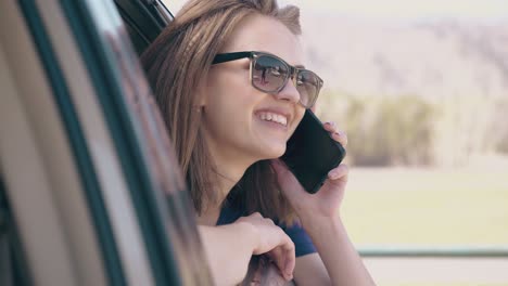 Señora-Sonriente-Con-Teléfono-Mira-Por-La-Ventana-Abierta-Del-Automóvil