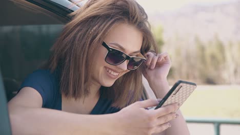 girl-scrolls-news-feed-on-phone-leaning-out-of-car-closeup