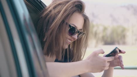 nice-girl-looks-at-phone-sitting-in-car-at-lawn-slow-motion