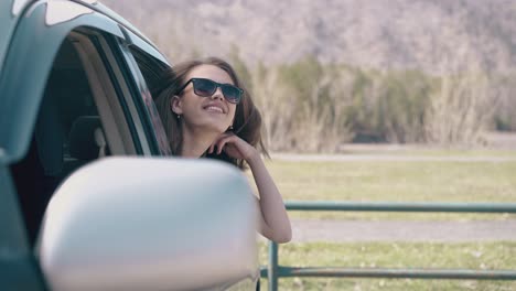 lady-in-sunglasses-fixes-hair-leaning-out-of-car-at-field