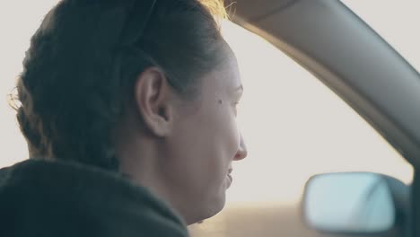 dark-haired-woman-talks-driving-car-at-bright-sunset-light