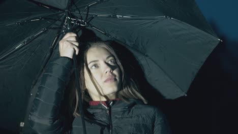 smiling-woman-holds-umbrella-under-night-rain-slow-motion