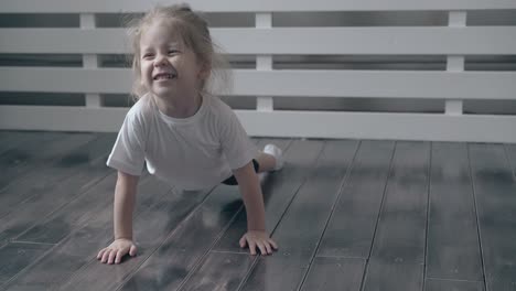 sweet-blond-toddler-does-exercises-on-wooden-floor