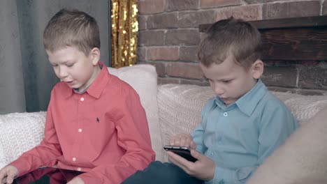 boy-holds-tablet-on-knees-near-brother-playing-on-smartphone