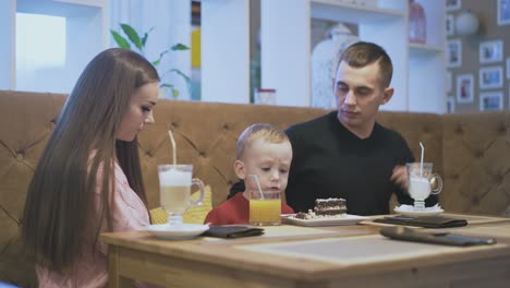 lucky-parents-enjoy-sitting-on-sofa-at-wooden-table-in-cafe