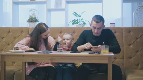 exciting-child-talks-to-mother-sitting-near-father-in-cafe