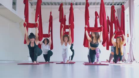women-stretch-legs-holding-red-aerial-fly-yoga-hammocks