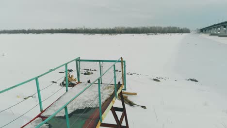 Muelle-Oxidado-Se-Encuentra-En-Un-Río-Congelado-Con-Un-árbol-Caído-En-La-Nieve.
