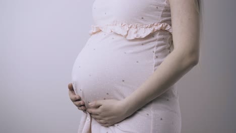 pregnant-woman-in-pink-frock-stands-near-white-wall-closeup