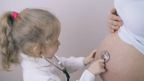 Mädchen-Mit-Stethoskop-Streichelt-Schwangeren-Mama-Bauch-Zu-Hause