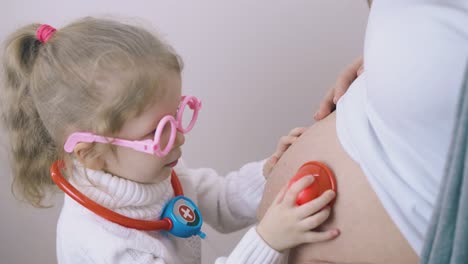 Kind-Mit-Spielzeugstethoskop-Spielt-Arzt-Mit-Schwangerer-Mama