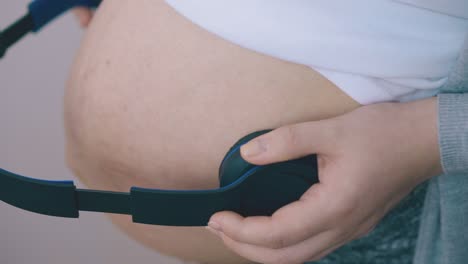 pregnant-woman-puts-headphones-to-tummy-in-room-closeup