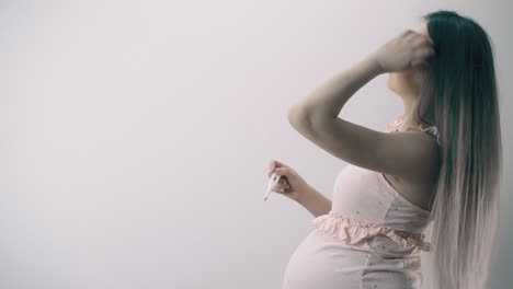 pregnant-lady-looks-at-digital-thermometer-by-white-wall