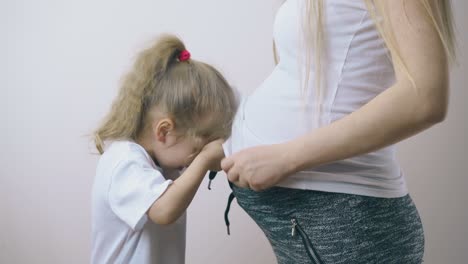 Kleines-Mädchen-Versucht-Sich-Unter-Dem-T-Shirt-Der-Schwangeren-Mutter-Zu-Verstecken