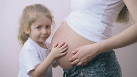 girl-kisses-large-tummy-of-pregnant-mummy-listening-to-baby