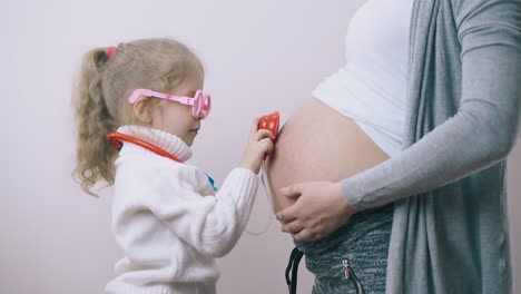 Mädchen-Berührt-Schwangeren-Mama-Bauch-Mit-Spielzeugstethoskop