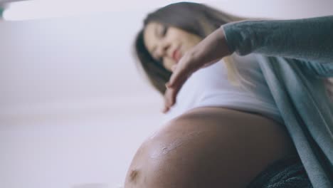 Mujer-Embarazada-Dibuja-Sol-Con-Crema-En-La-Barriga-En-Una-Habitación-Iluminada