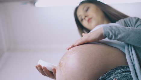 Schwangere-Frau-Trägt-Feuchtigkeitsspendende-Lotion-Auf-Den-Bauch-Auf,-Nahaufnahme