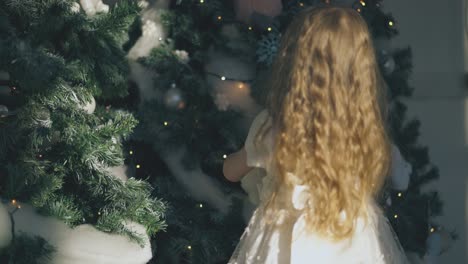 Kleines-Mädchen-Legt-Ausgestopftes-Kaninchen-Auf-Den-Weihnachtsbaum-Im-Zimmer