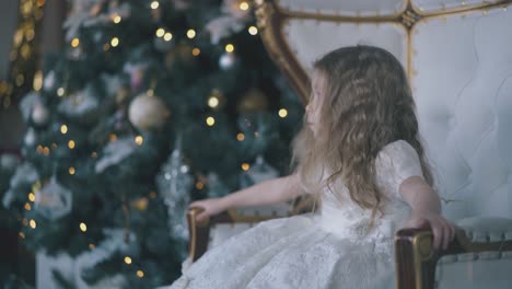 pretty-girl-sits-in-beautiful-armchair-near-Christmas-tree