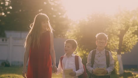 lady-in-red-dress-walks-holding-children-with-school-bags