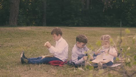 little-boy-eats-burger-sitting-on-grass-near-classmates