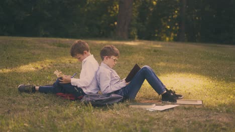 schoolboys-read-books-sitting-on-green-lawn-after-lessons