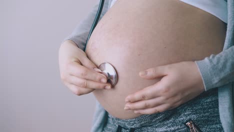 La-Mujer-Embarazada-Escucha-Los-Latidos-Del-Corazón-Del-Bebé-En-La-Vista-Cercana-De-La-Pared.
