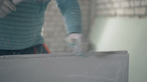 worker-holds-gypsum-plasterboard-and-beats-with-hammer