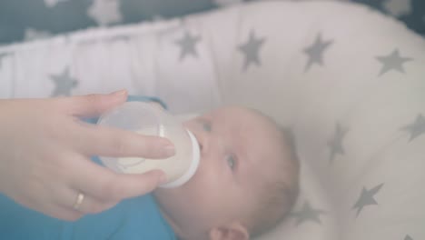 mommy-holds-bottle-feeding-little-son-with-milk-mix-in-cot