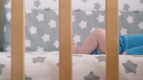 Neugeborenes-Kind-Liegt-In-Einem-Hölzernen-Kinderbett-Mit-Sternenverzierter-Bettwäsche