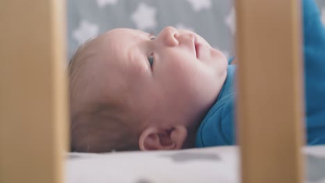 Süßes-Baby-Mit-Blauen-Augen-Berührt-Gesicht-Mit-Der-Faust-Im-Kinderbett