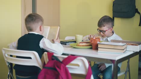 little-boy-reads-book-with-friend-eating-pizza-in-canteen