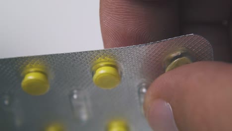 man-holds-blister-with-yellow-pills-above-light-background