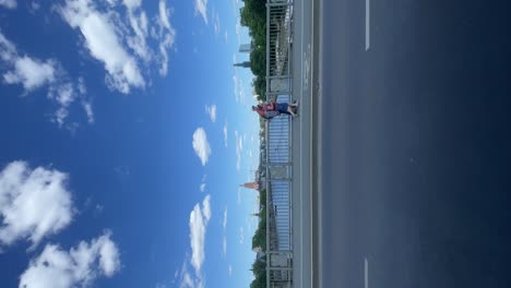 Driving-Past-People-Walking-Along-Bridge-In-Frankfurt-On-Sunny-Day-With-Blue-Skies