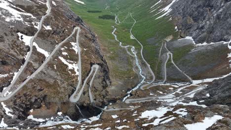 Tilt-up-aerial-from-Trollstigen-Snowy-Peaks-and-winding-roads-to-Istedalen-valley-leading-to-Rauma-and-Andalsnes---Norway-Epic-Aerial-Journey
