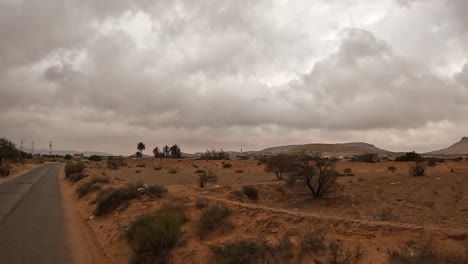 Traveling-by-car-through-arid-landscape-of-Tunisia-on-cloudy-stormy-day,-driver-point-of-view