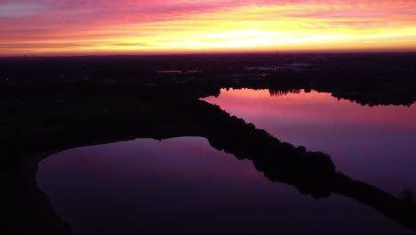 A-drone-is-high-above-pink-gold-and-purple-reflecting-waters-at-sunset-in-Mechels-Broek-near-Antwerp,-Belgium