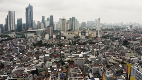 Aerial-forward-shot-over-Indonesian-suburb-neighborhood-and-Skyline-of-Jakarta-Downtown-in-background,-Indonesia