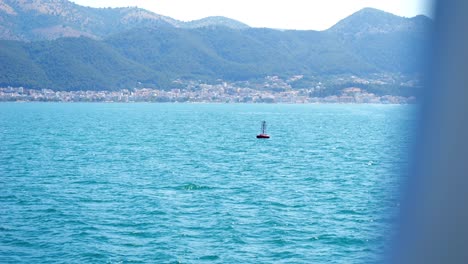 Green-buoy-floating-on-the-blue-waters-of-the-Ionian-Sea,-with-the-coast-of-Greece-in-the-background