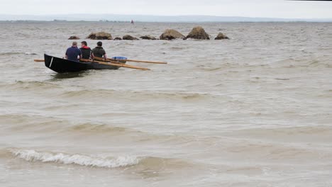 Tripulación-De-Tres-Personas-Reman-Y-Las-Olas-Los-Hacen-Girar-En-Un-Barco-Currach.