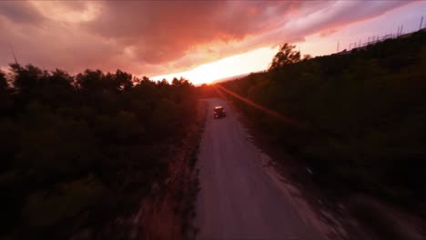 FPV-aerial-following-an-SUV-driving-along-a-mountain-road-into-the-scenic,-orange-sunset